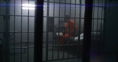 Turuncu üniformalı Afro-Amerikan mahkum yatakta oturur, hücrede İncil okur. Erkek suçlu, hapis ya da gözaltı merkezinde hapis cezasına çarptırıldı. Tanrı 'ya inan. Çubuklardan göster.