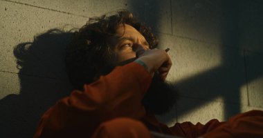 Turuncu üniformalı bunalımlı bir mahkum hapishane hücresinde yatağında sigara içiyor. Suçlu, mahkum hapiste suçtan hapis cezasına çarptırıldı. Güneş parmaklıklı pencereden parlıyor. Cezaevi.