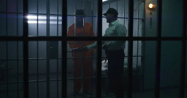 刑務所の警官は 刑務所内のオレンジ色の制服を着た男性の囚人に聖書を贈った 刑務所では刑務所で有罪判決が下される 拘禁センターまたは矯正施設 金属棒を通して見る — ストック写真
