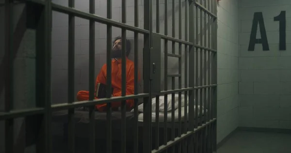 Więzień Pomarańczowym Mundurze Siedzi Łóżku Czyta Biblię Celi Oficer Więzienny — Zdjęcie stockowe