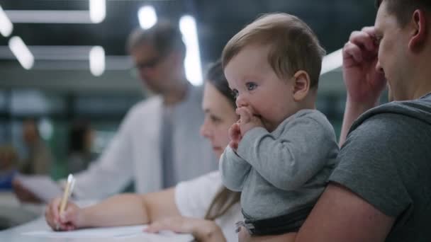 Bělošská Rodina Dětmi Stojí Recepci Hale Kliniky Žena Vyplňuje Dokumenty — Stock video
