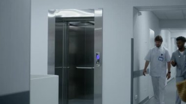 Afrikalı Amerikalı doktor iş arkadaşıyla asansör kapısına gelir ve çağrı düğmesine basar. Sağlık çalışanları, sağlık merkezi koridorunda asansör bekliyor. Hastanede çok ırklı sağlık uzmanları çalışıyor.
