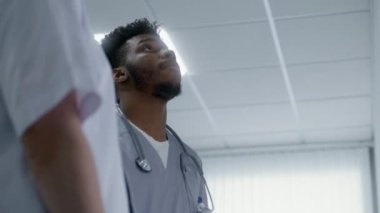 Sağlık uzmanı klinik koridorundaki asansörü arıyor. Afro-Amerikalı doktor başka bir sıhhiyeciyle hasta ya da tıbbi test sonuçlarını tartışıyor. Doktorlar hastane koridorunda duruyor..
