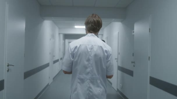 ホワイトユニフォームの医療専門家が医療センターの廊下を歩いています 医師は患者と面会する クリニックの廊下で働く医療関係者 スローモーション トラッキングショット バックビュー — ストック動画