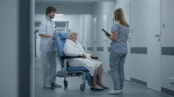 Erkek Hemşire Kadın Hastayla Birlikte Klinik Koridorunda Tekerlekli Sandalye Itiyor — Stok video