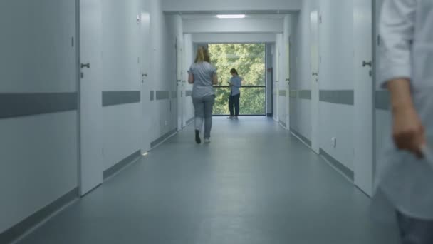 クリニックの廊下 医師とプロのメディクスが歩きます デジタルタブレット付きの看護師は 窓の近くに立っている女性の患者に来ます 現代の病院や医療センターの廊下の医療スタッフや患者 — ストック動画