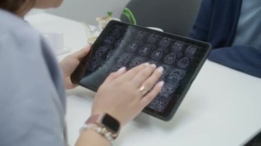 Kadın doktor, klinikteki kafede hastasıyla oturuyor. Sağlık uzmanı dijital tablet kullanır, MRI veya CT görüntülerini izler, insanlarla konuşur. Hastane veya tıp merkezi kafeteryasında tıbbi personel.