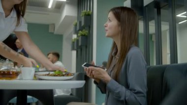Kadın klinikteki masada oturuyor, telefon kullanıyor. Kafeterya çalışanı kadın ziyaretçiye yemek getiriyor. Tıp personeli, doktorlar ve hastalar modern tıp merkezinde veya hastane yemek odasında yemek yerler..
