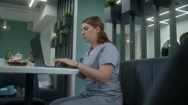 女医生坐在诊所的咖啡店里 用笔记本电脑 医疗专家在网上与病人交流 检查医疗检测结果或上网 医护人员在医院餐厅工作 — 图库视频影像