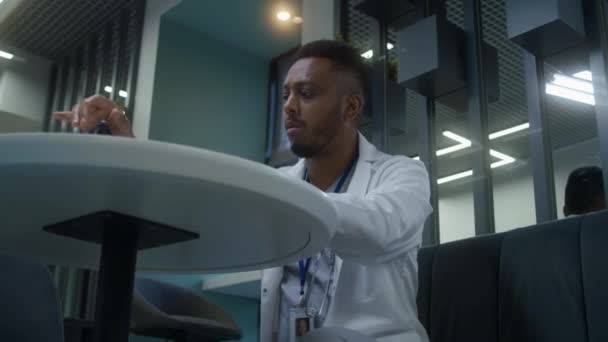 非裔美国医生坐在诊所的咖啡店里 医疗专家在数字平板电脑上工作 观察病人的医疗检测结果 医院或医疗中心食堂的医务人员 — 图库视频影像