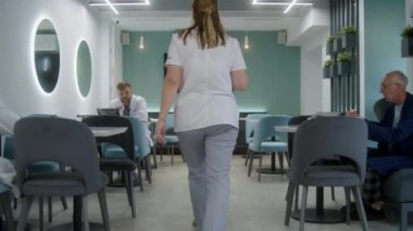 Kadın doktor hastane kafesine gelir ve iş arkadaşının yanına oturur. Doktor yemeğini yer ve başka bir doktorla konuşur. Kadınlar klinik kafeteryasında kanepede oturur ve telefonunu kullanırlar. Sağlık personeli ara verdi..