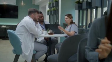 Çok ırklı doktorlar klinikte oturup dizüstü bilgisayar kullanıyorlar. Profesyonel doktorlar konuşur, hastaların tıbbi test sonuçlarını inceler, teşhisi tartışırlar. Hastane veya tıp merkezi kafeteryasında çalışan tıbbi personel.