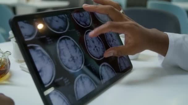 非洲裔美国医生在临床咖啡馆里翻阅数字平板电脑上的Mri或Ct扫描图像 专业医生检查病人脑部扫描结果 医院餐厅 靠近点 — 图库视频影像