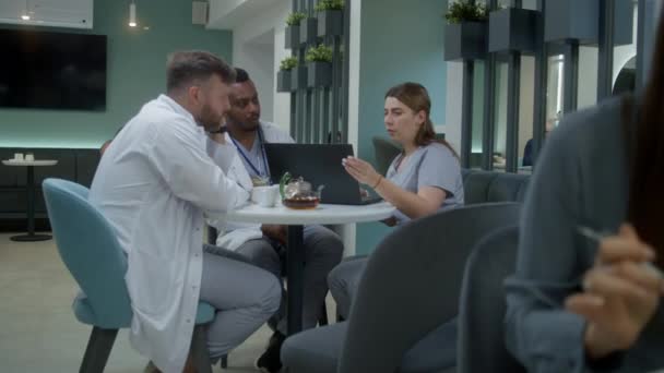 Médicos Multiétnicos Sientan Cafetería Clínica Usar Computadora Portátil Los Médicos — Vídeos de Stock