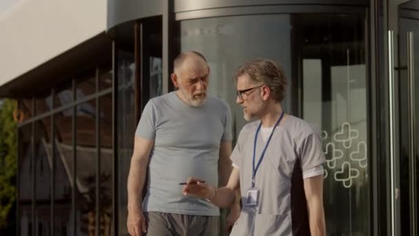 Reifer Arzt Mit Digitalem Tablet Der Hand Steht Mit Älteren — Stockvideo