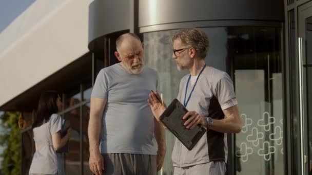 Ώριμος Ιατρός Ψηφιακή Ταμπλέτα Στα Χέρια Στέκεται Ηλικιωμένο Ασθενή Στην — Αρχείο Βίντεο