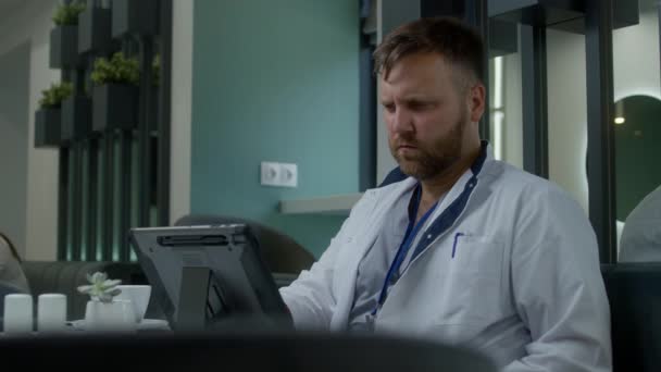 成年医生坐在医院自助餐厅里喝咖啡 医学博士使用数字平板电脑学习Mri或Ct扫描结果 医务人员在医疗中心餐厅休息 保健系统 — 图库视频影像