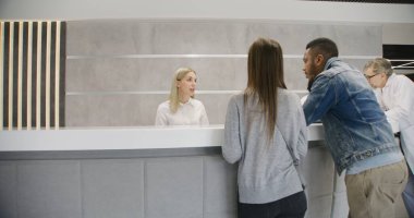 Klinik girişinde resepsiyon masasının yanında duran çok ırklı çift doktorla randevu alıyor. Bayan yönetici danışma masasında hastalarla konuşuyor. Modern hastanede tıbbi personel işi..