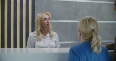 Klinik lobisindeki resepsiyon masasının yanında yaşlı çift duruyor. Doktorla randevuya gelin. Bayan yönetici danışma masasında hastalarla konuşuyor. Modern hastanede tıbbi personel işi..