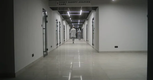 Doctors, healthcare professionals and patients walk along the bright clinic corridor. Medical staff and people in private hospital or modern medical center. Laboratory or emergency station. Back view.