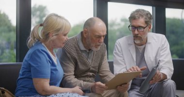 Yaşlı çift, doktorla görüştükten sonra klinik lobisindeki kanepede oturuyor. Doktor konuşur, tıbbi muayene ya da test sonuçlarını tartışır. Modern tıp merkezinde bekleme odası. Sağlık hizmetleri sistemi.