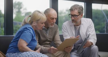 Yaşlı çift, doktorla görüştükten sonra klinik lobisindeki kanepede oturuyor. Doktor konuşur, tıbbi muayene ya da test sonuçlarını tartışır. Modern tıp merkezinde bekleme odası. Sağlık hizmetleri sistemi.