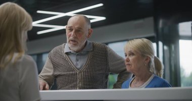 Klinik lobisindeki resepsiyon masasının yanında yaşlı çift duruyor. Doktorla randevuya gelin. Kadın resepsiyonist danışmadaki hastalarla konuşuyor. Modern hastanede tıbbi personel işi..