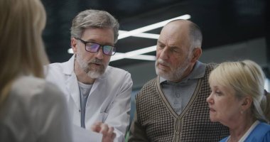 Tıp merkezinin bekleme odasındaki resepsiyonun yanında duran yaşlı çift doktordan randevu alıyor. Olgun doktor danışmadaki hastalarla konuşur. Modern klinikte tıbbi personel.