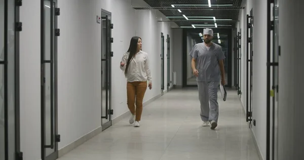 Medical worker, male nurse leads Asian woman along the clinic corridor for appointment with doctor, examination or tests. Medical staff and patient in hospital ot medical center. Healthcare system.