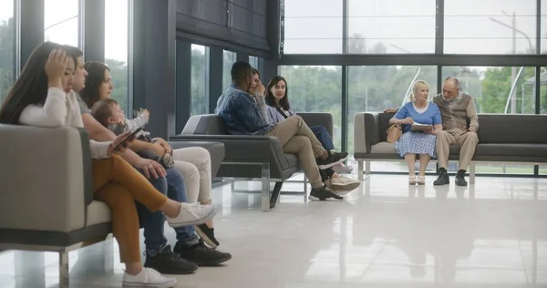Diverse multiethnic people sit on couches in clinic lobby area, wait for appointment with doctor or medical test results. Waiting area in medical center with modern design. Healthcare system.
