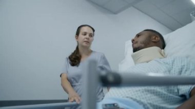 Yaralı Afrikalı Amerikalı hasta sedyede boyunluk takarak oturuyor ve hemşireyle konuşuyor. Profesyonel sıhhiyeciler orta yaşlı adamı sedyeyle hastane koridorunun aşağısındaki hastaneye götürdüler..