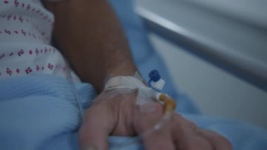 Yaşlı adam elinde venöz sondayla sedyede yatıyor. Sağlık uzmanı sedyedeki yaşlı hastayı sağlık merkezi koridorundan ameliyathaneye götürüyor. Hastanede çalışan tıbbi personel. Kapat..