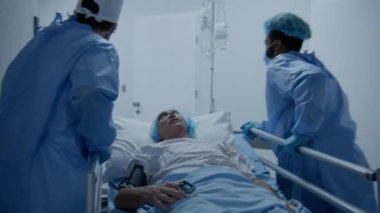 Cerrahlar, kıdemli hastayı klinik koridorundan ameliyathaneye naklederler. Sıhhiye hastaları olan diğer doktorlar için kapıları açar. Yaşlı adam sedyede yatıyor. Damlalar altında ve nabız oksimetresi parmağında..