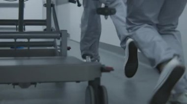 Hemşireler ve sağlık görevlileri koşar, ağır yaralı bir hastayla sedyeyi ameliyathaneye götürün. Sıhhiyeciler insan hayatını kurtarır. Tıbbi personel bacaklarını kapatın. Parlak tıbbi tesis koridoru. Yavaş çekim.