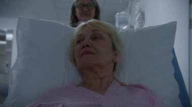 Kıdemli kadın sedyede yatıyor, olgun kadın doktorla konuşuyor. Doktor, hastayı ameliyattan sonra hastane koğuşuna naklediyor. Hastanede çalışan tıbbi personel..