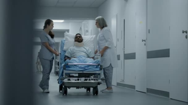 成熟的医生和护士带着受伤的病人走在诊所的走廊上 医生们把戴着颈架的非裔美国人送到医院病房 在医疗中心工作的医务人员 — 图库视频影像