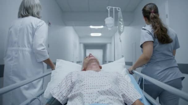 女医生和护士沿着医院走廊走着 把老年病人推送到医院病房 老年人躺在血淋淋的壁炉架上 用呼吸管滴着 现代诊所的医务人员 — 图库视频影像