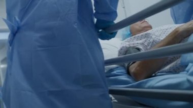 Çok ırklı cerrahlar, yalancı yaşlı bir adamı ameliyat odasından sedye ile çıkarıyorlar. Hemşire ve sağlık görevlileri hemen tıbbi tesisin koridorlarını kapatın. Acil serviste personel işi. Yavaş çekim.