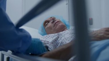 Yaşlı bir adam tıbbi tesis koridorunda sedyede yatıyor. Doktor ağır hasta muayenesi yapıyor ve kan basıncını ölçüyor. Personel acil servisi. Ağır çekim. Kapat..