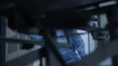 Kadın doktor diğer sağlık görevlilerinin ameliyat bloğu için kapıyı açar. Cerrahlar, kıdemli hastayı klinik koridorunun aşağısındaki ameliyathaneye naklederler. Yaşlı adam damlalar altında sedyede uyuyor. Tıbbi personel iş başında..