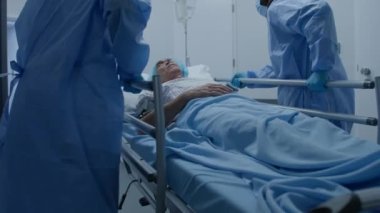 Çok ırklı cerrahlar sedyeyi çok hasta bir adamla ameliyat odasından iterler. Hemşire ve sağlık görevlileri tıbbi tesisin koridorlarını kapatın. Acil serviste personel işi. Yavaş çekim.
