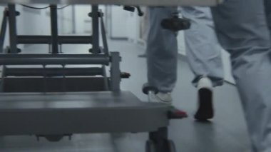 Doktorlar ve sağlık görevlileri, ağır yaralı hastalarla birlikte sedyeyi ameliyathaneye götürün. Sıhhiyeciler insan hayatını kurtarır. Tıbbi personelin bacaklarını kapatın. Parlak tıbbi tesis koridoru. Yavaş çekim.