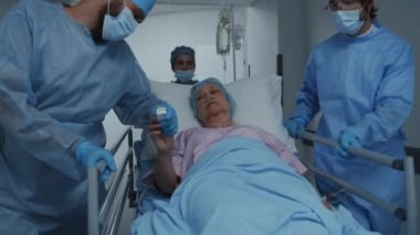 Doktorlar ve sağlık görevlileri yaşlı kadınla birlikte sedyeyi ameliyathaneye götürün. Doktor hasta elinin nabzını kontrol ediyor. Sağlık personeli acil serviste çalışıyor. Ön manzara. İzleme görüntüsü.