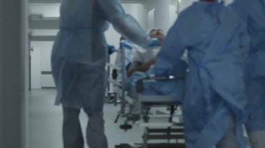 Doktorlar ve hemşireler yaralı bir hastayla birlikte sedyeyi ameliyathaneye götürürler. Profesyonel sağlık görevlileri acil serviste insan hayatını kurtarıyor. Tıbbi tesis koridoru. Arkadan bak. Yavaş çekim.
