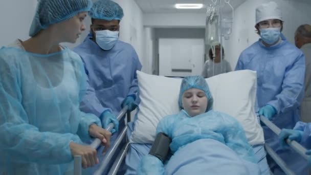 护士和母亲的孩子推担架与生病的年轻女孩到手术室 女人支持躺在Gurney的女儿身上医护人员在急诊室工作 跟踪目标慢动作 — 图库视频影像