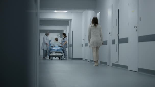 颈部支撑架受伤的病人躺在医院走廊的绞刑架上 专业医护人员站在医疗中心走廊中央 与非裔美国人谈论健康问题 工作的医务人员 — 图库视频影像
