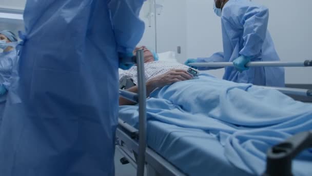 多民族外科医生将老年卧床病人推离手术室 护士和辅助医务人员关闭医院走廊大门 医护人员在急诊室工作 慢动作 — 图库视频影像