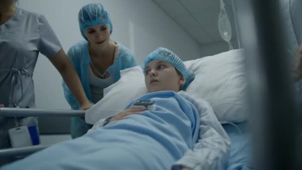 医学界在医疗中心走廊下经手术后把病人送到医院病房 小女孩躺在Gurney床上 看着手指上的脉搏血氧计 然后和妈妈说话 工作的医务人员 — 图库视频影像