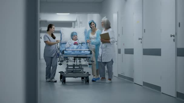 女医生在手术前咨询躺在担架上的孩子 护士和母亲在医疗设施走廊里推着Gurney和小女孩 急诊室走廊工作的医务人员 — 图库视频影像