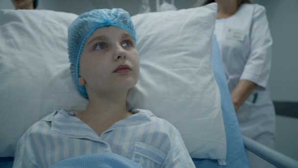小女孩坐在Gurney上环顾四周 专业的医生沿着医疗中心走廊走着 术后把病人的骨科医生推送到医院病房 在现代诊所工作的医务人员 — 图库视频影像